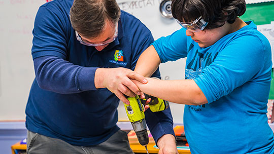 Gersh Academy Teacher Instructing a Student How to Drill a Screw Into Wood During Vocational Training