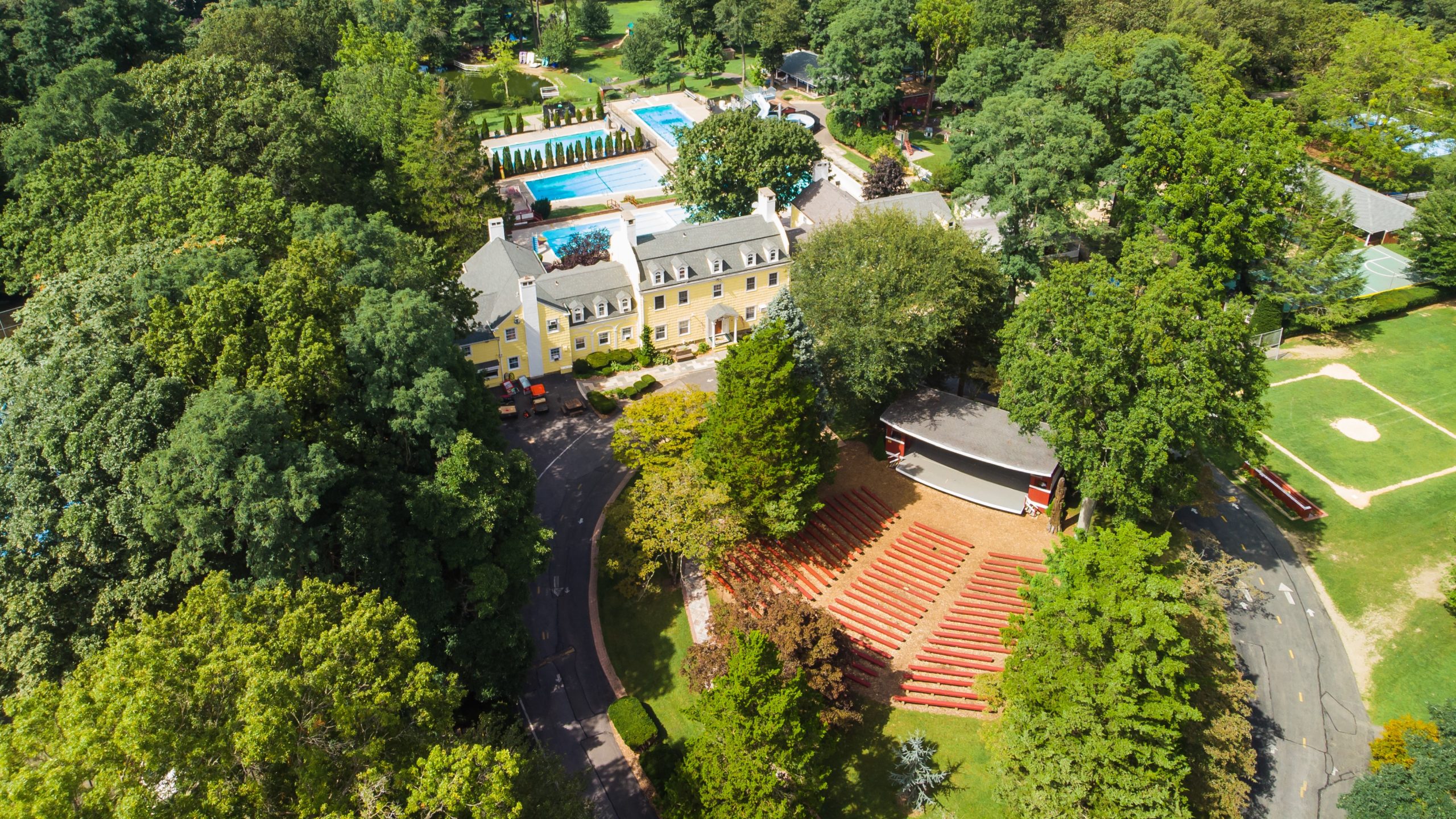An aerial photo of green lawns and trees around an outdoor theater, swimming pools and a school building!